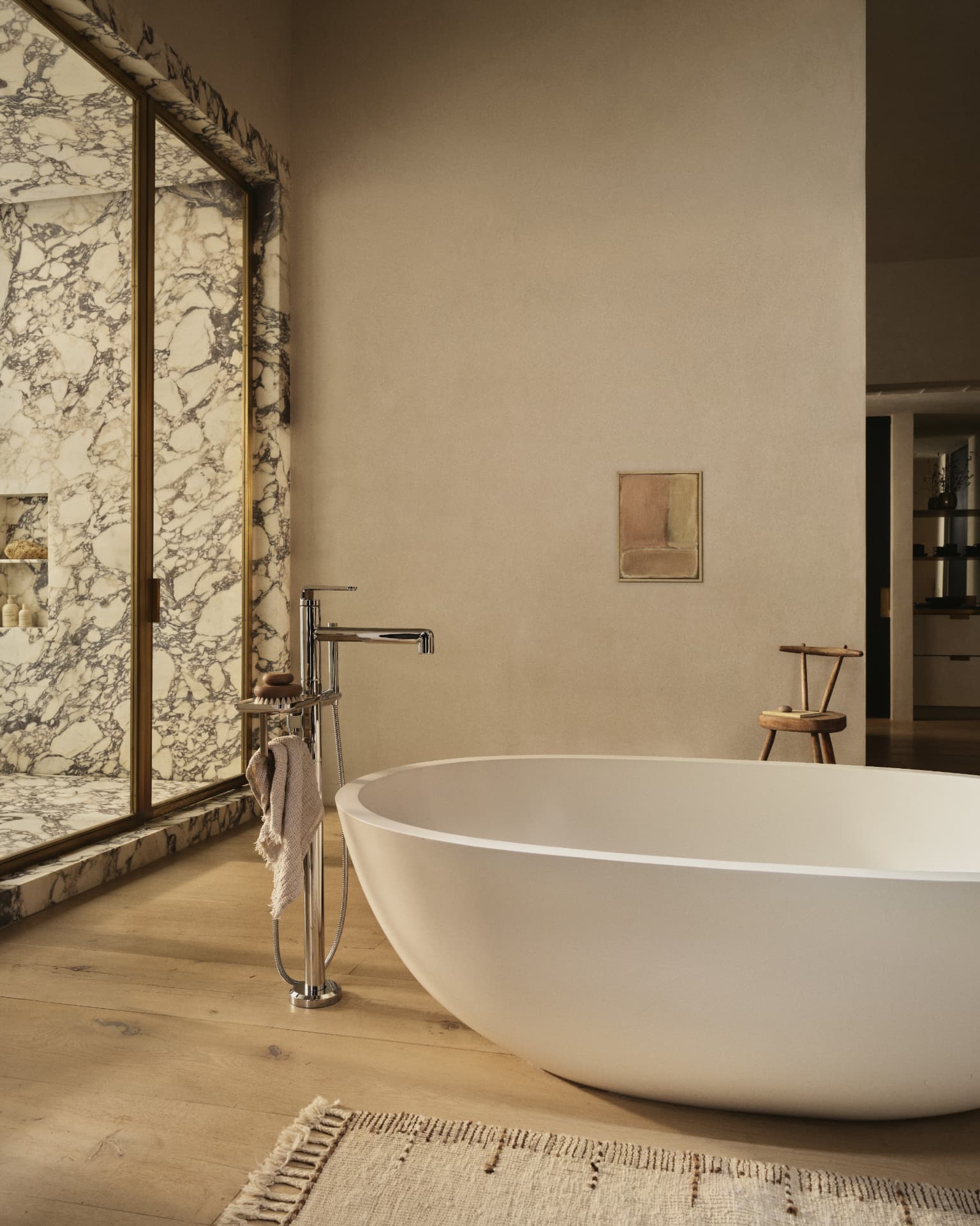 Freestanding bath beside a richly veined marble wall and polished floor-mounted faucet